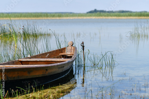 Fragment of wooden fishing boat on the lake with transparent blue sky and clear water.