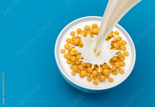 Corn balls with pouring milk on blue background, top view