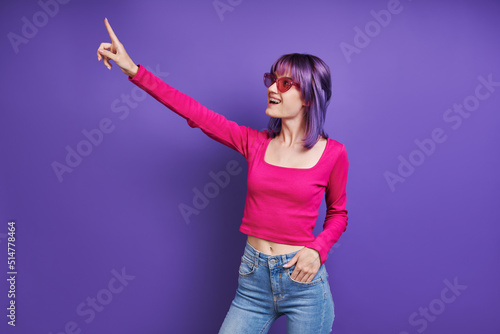 Cheerful young woman pointing away while standing against purple background © gstockstudio