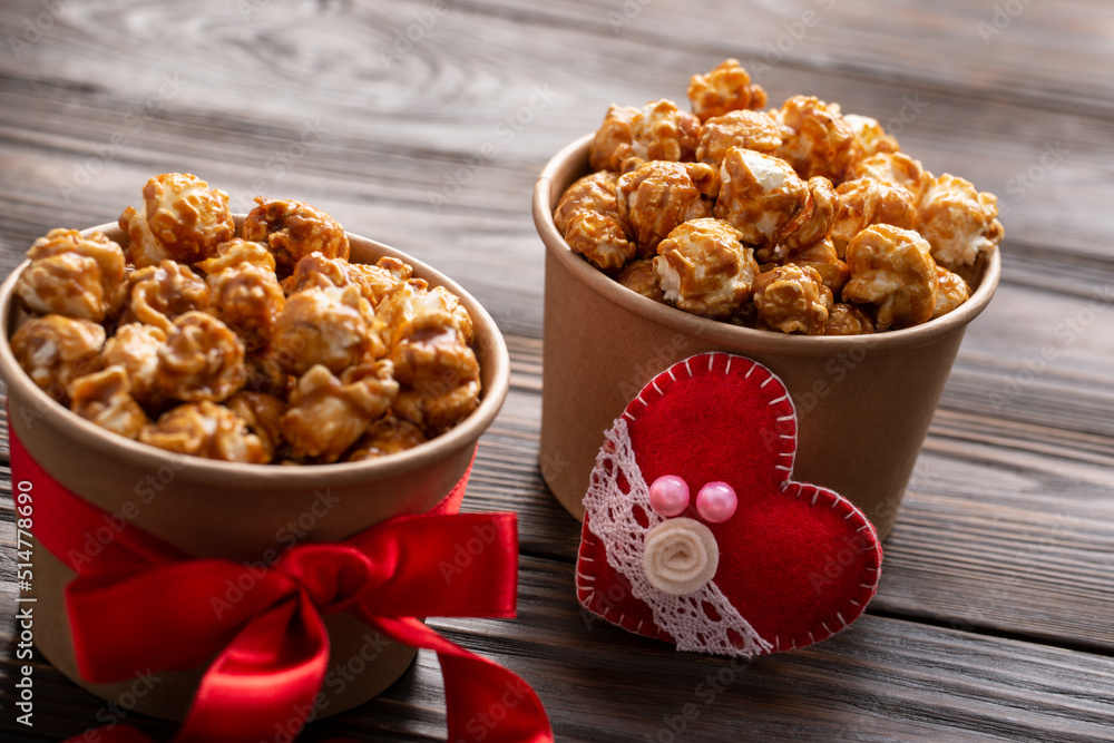 Carton buckets with caramelized popcorn and valentine decorations on kitchen table food background