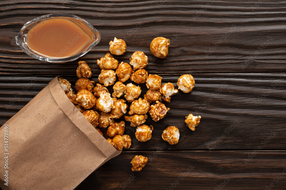 Caramelized popcorn in paper bag on wooden kitchen table flat lay
