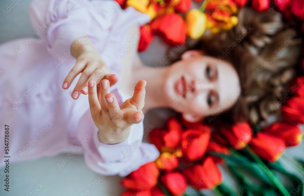 A young woman is lying on the floor among red tulips. The concept of March 8, Valentine's Day. Spring portrait of a woman.Focus on the girl's hands, in the foreground.