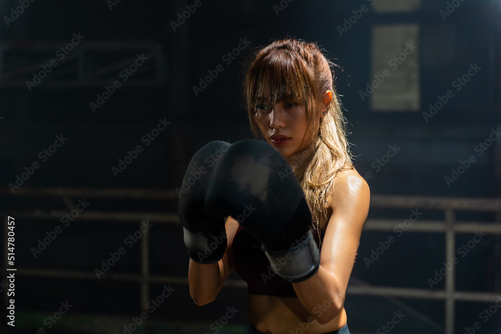 Fototapeta premium Portrait of Active Asian woman wraps her hands with boxing bandages and do kickboxing fighting exercise in abandoned building. Healthy female athletic do sport workout training alone in dark old gym