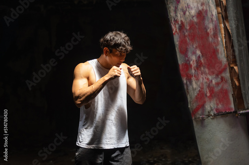 Strong Asian sportsman athlete do combat sport training workout boxing exercise with punching the air in abandoned building. Active man boxer practicing fighting exercise kickboxing in dark old gym
