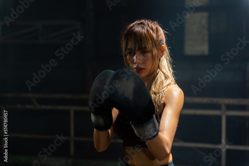 Portrait of Active Asian woman wraps her hands with boxing bandages and do kickboxing fighting exercise in abandoned building. Healthy female athletic do sport workout training alone in dark old gym