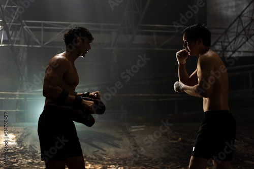Billede på lærred Strong Asian sportsman practicing boxing workout punching with male combat sport trainer in abandoned building