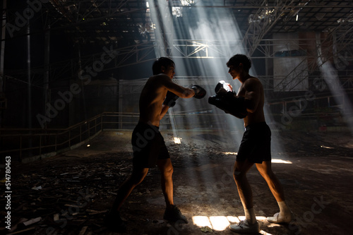 Photo Strong Asian sportsman practicing boxing workout punching with male combat sport trainer in abandoned building