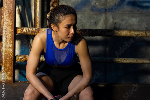Asian sportswoman do sport workout weight training exercise in abandoned building. Active woman bodybuilder athlete practicing muscular strength bodybuilding lifting heavy dumbbell in dark old gym