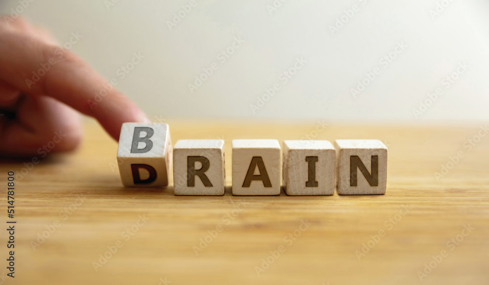 Brain drain concept. Finger flips letter at wooden cube changing the word brain to drain. Stock