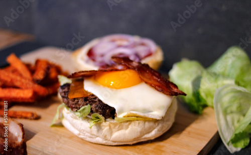 Burger w artystycznej kompozycji z frytkami i batatami oraz cebulą pieczarkami. Burgerownia - zdjęcie świeżego, apetycznego burgera