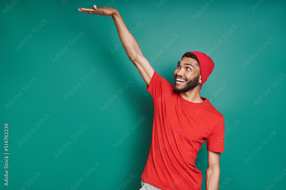 Fototapeta premium Handsome African man showing height and smiling while standing against green background