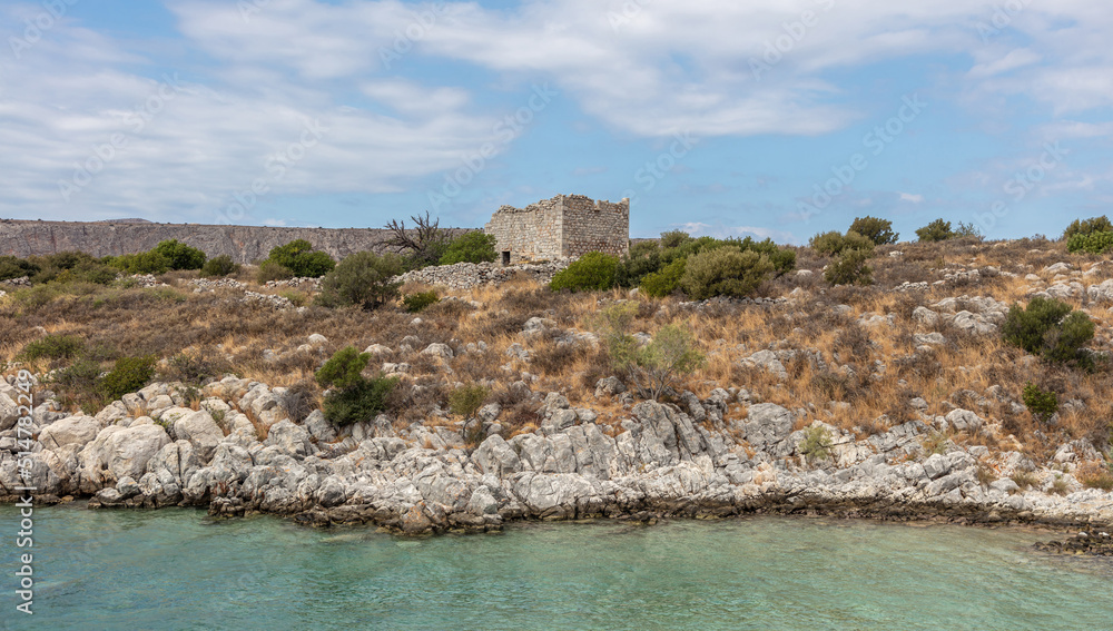 Greece. Mani Laconia, Peloponnese. Ruin old stone building on rocky land, calm sea, cloudy blue sky.