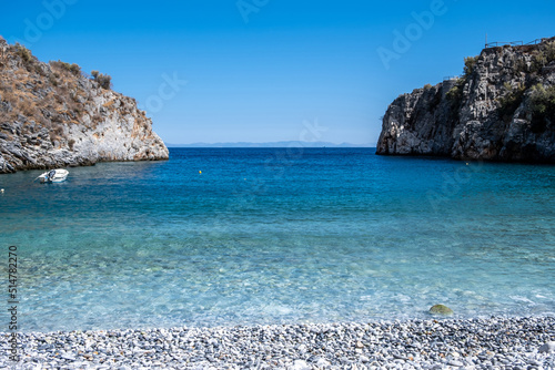 Greece. Pebble beach, moored boat in calm sea, Mani Laconia, Peloponnese crystal clear water.