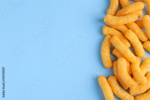 Heap of tasty cheesy corn puffs on light blue background, flat lay. Space for text