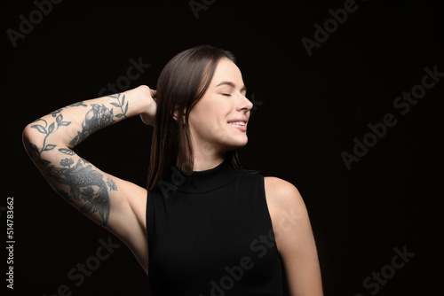 Beautiful woman with tattoos on arm against black background