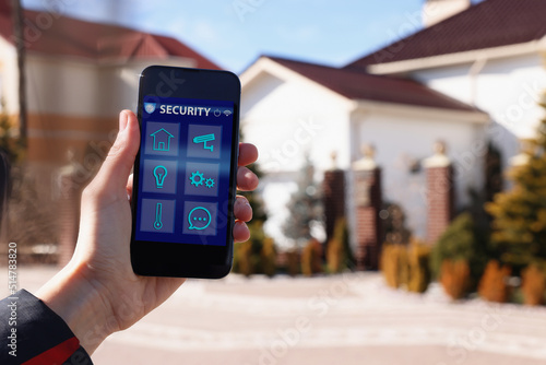 Woman using home security app on smartphone outdoors, closeup