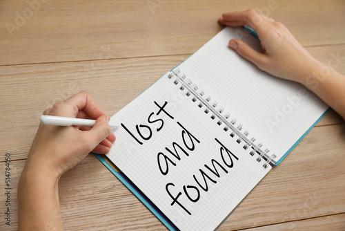 Woman writing phrase Lost and Found in notebook at wooden table, closeup