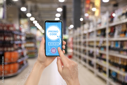 Woman holding smartphone with activated promo code in supermarket, closeup