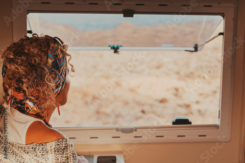 Back view of traveler woman looking outside the camper van window. Van life and travel people lifestyle. Freedom living off grid in a vehicle and alternative house on wheels. Concept of life photo