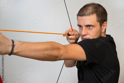Young boy using a toy bow. The bow is red and the arrow is orange. Caucasian white man with short hair, little beard and black eyes on a white background