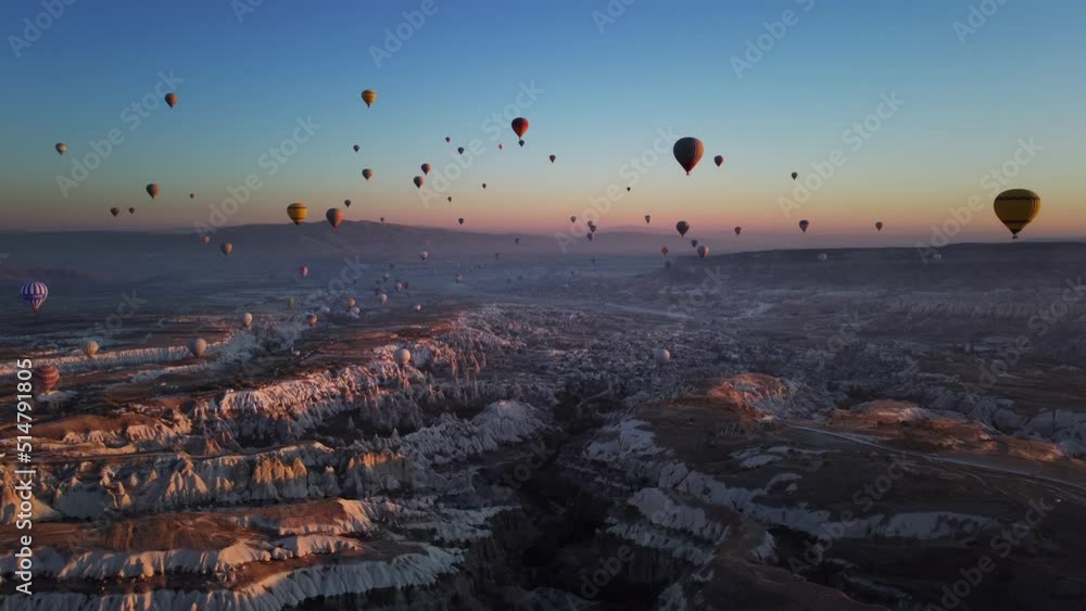 Idyllic scenery of Cappadocia valley and lots of flying hot air balloons over volcanic hills at summer morning. Drone landscape of a terrain with limestone rocks and levitating transport with baskets. Idyllic scenery of Cappadocia valley and lots of flying hot air balloons over volcanic hills at summer morning. Drone landscape of a terrain with limestone rocks and levitating transport with baskets.