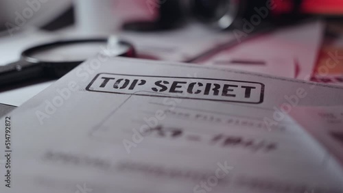 Close up top secret stamped document with magnifying glass next to it on desk. Leaked sensitive paper in dark room or military or government agency or spy network. Classified information in text photo
