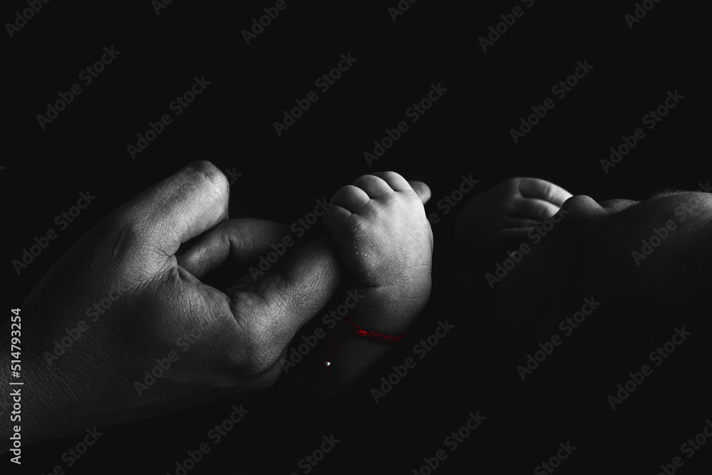 Baby holds the parents finger in hand. Black white silhouette photo. Red band for luck on baby hand. Studio black background. Lovely family memories. Baby holds the parents finger in hand. Black white silhouette photo. Red band for luck on baby hand. Studio black background. Lovely family memories.