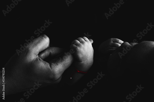 Baby holds the parents finger in hand. Black white silhouette photo. Red band for luck on baby hand. Studio black background. Lovely family memories.