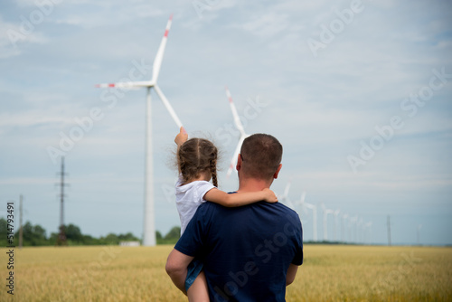 A girl and her dad look at the wind generator in the field. Ecology. Future.