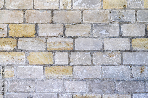 An old damaged wall made of white, gray and yellow bricks as a background