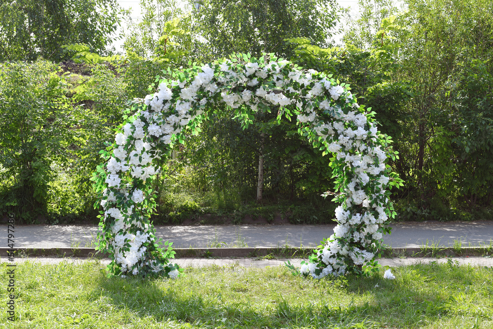 Fototapeta premium Decoration wedding arch with white flowers on a green natural background. Beautiful wedding ceremony outdoors.