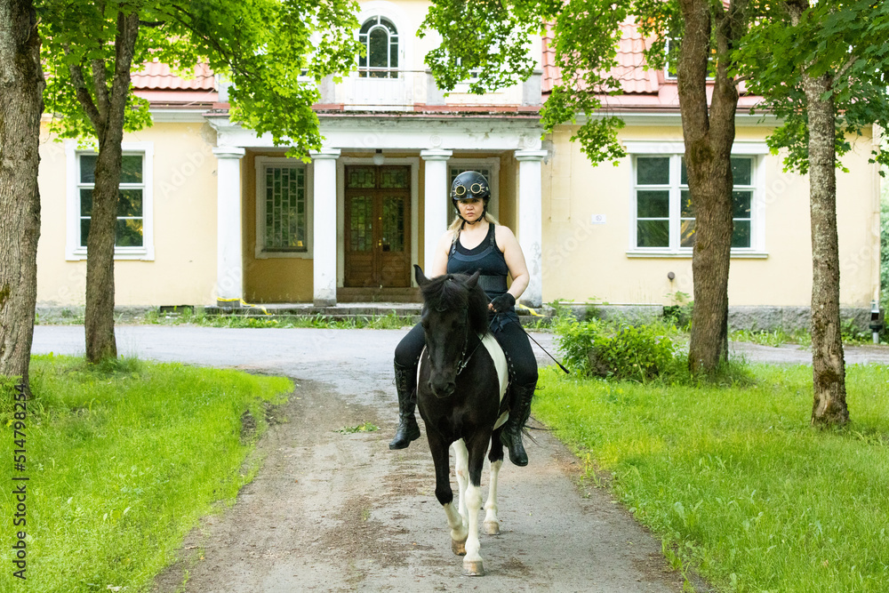 Steampunk female rider with Icelandic horse. Rider has driving glasses and black helmet. Black and white horse. Steampunk female rider with Icelandic horse. Rider has driving glasses and black helmet. Black and white horse.