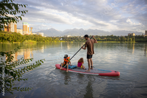 dad rides the kids on a sap board. children in life jackets.active sports life. water sports