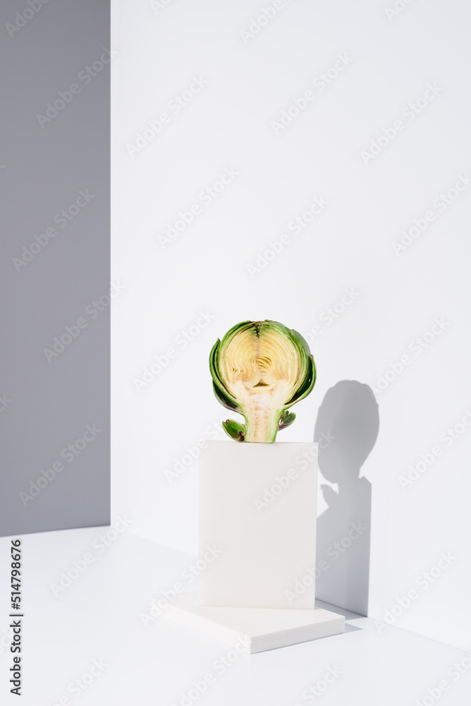 Una alcachofa partida por la mitad sobre un soporte blanco y fondo gris Una alcachofa partida por la mitad sobre un soporte blanco y fondo gris