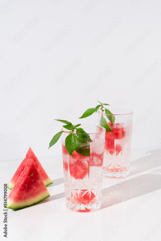 Dos vasos de zumo de sandía con trozos de sandia y hielo sobre fondo claro Dos vasos de zumo de sandía con trozos de sandia y hielo sobre fondo claro