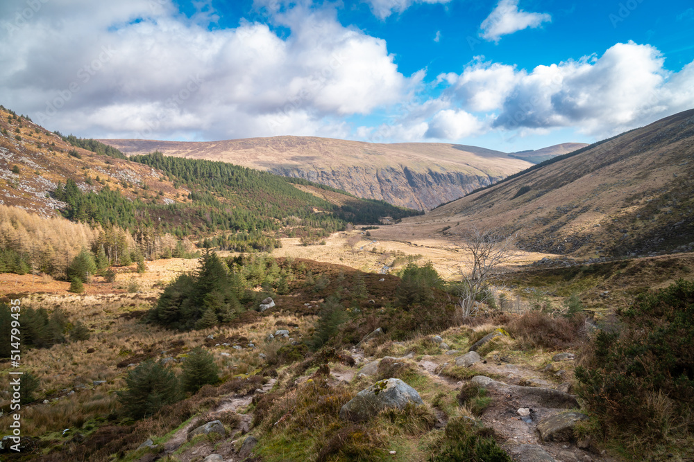Panoramic view of Glenmalure valley during sunny day. It is glacial valley in the Wicklow Mountains in Ireland. Base for accessing the mountain of Lugnaquilla. Saturated colors and dramatic sky. Panoramic view of Glenmalure valley during sunny day. It is glacial valley in the Wicklow Mountains in Ireland. Base for accessing the mountain of Lugnaquilla. Saturated colors and dramatic sky.