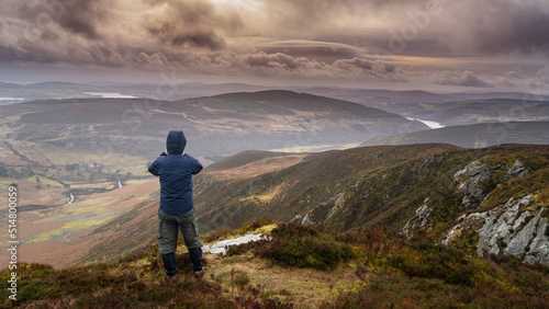 Man from behind looking towards Lough Tay (Guinness Lake) from Luggala peak in the Wicklow mountains Ireland. Cloudy and wet day