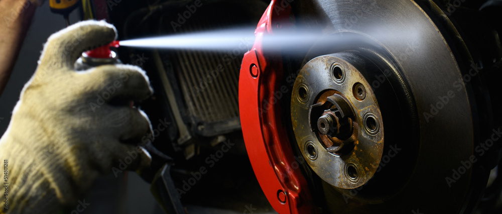 banner shot of auto mechanic spraying disc brake liquid on wheel near lamp in garage banner shot of auto mechanic spraying disc brake liquid on wheel near lamp in garage