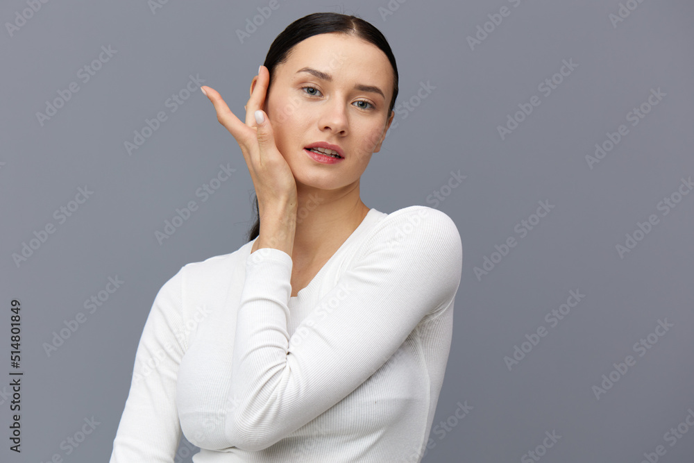 a beautiful, slender, elegant woman stands on a gray background in a white T-shirt with long sleeves and gently touches her neck with her fingers while looking at the camera, smiling pleasantly. a beautiful, slender, elegant woman stands on a gray background in a white T-shirt with long sleeves and gently touches her neck with her fingers while looking at the camera, smiling pleasantly.