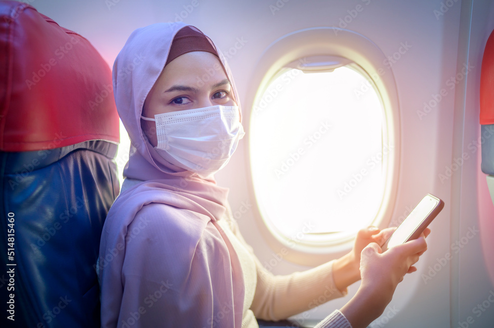 Young muslim woman with hijab wearing face mask onboard, New normal travel after covid-19 pandemic concept