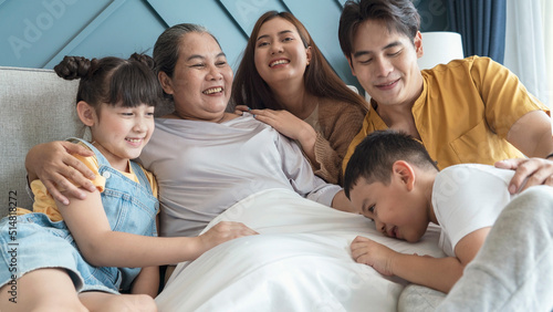 Grandma lay in bed feeling lonely, glad to see her son, daughter-in-law and granddaughter and young grandson hugging and laughing happily in the bedroom at home. Family and Relationships concept.
