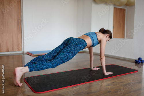 A sportswoman in sportswear is engaged in strength training in a sports club doing plank exercise.