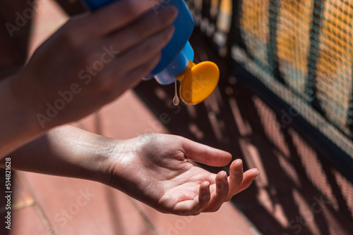 Detalle de las manos de una mujer echando protector solar con un bote azul de crema. Concepto de protegerse de los rayos UV en verano. photo