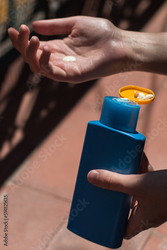 Imagen vertical de una mujer sosteniendo un bote de azul de protector solar con una gota crema en la mano. Concepto de protegerse de la exposición al sol en verano. photo