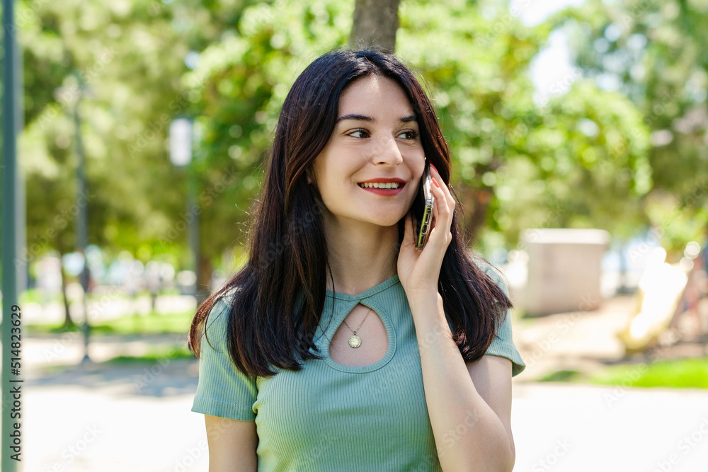 Happy woman wearing tee standing on city park, outdoors talking on mobile phone with friends or boyfriend with smiles. Happy woman wearing tee standing on city park, outdoors talking on mobile phone with friends or boyfriend with smiles.