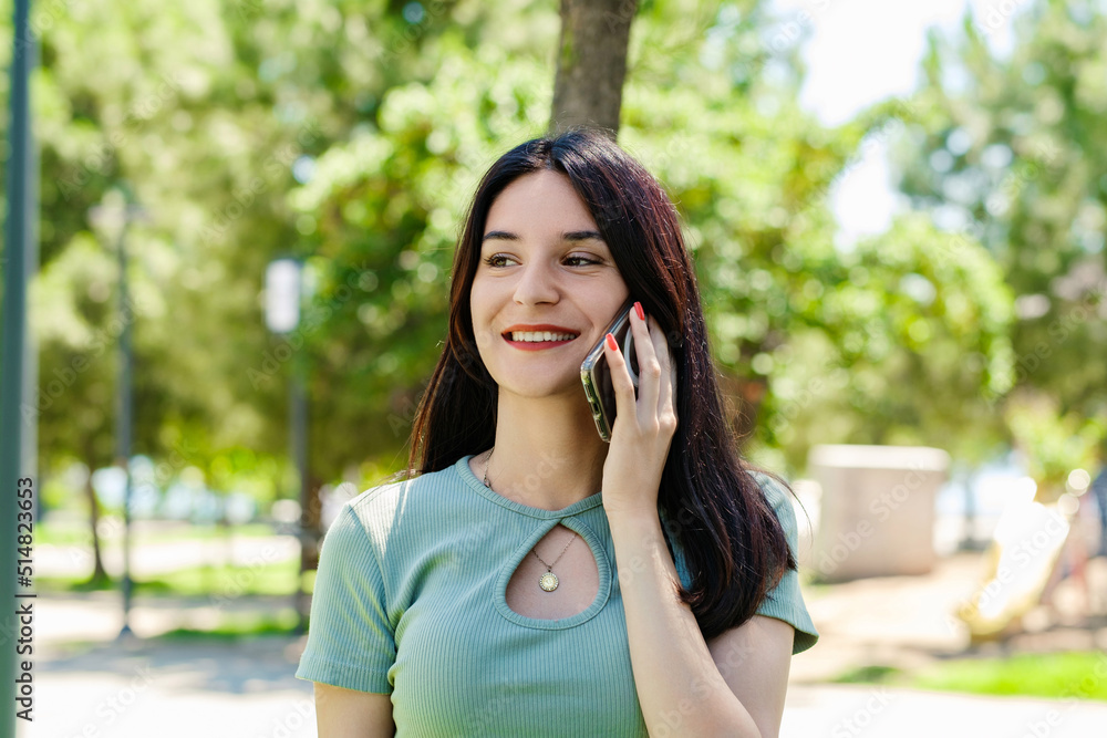 Cheerful brunette woman wearing tee standing on city park, outdoors talking on mobile phone with friends or boyfriend with smiles. Cheerful brunette woman wearing tee standing on city park, outdoors talking on mobile phone with friends or boyfriend with smiles.