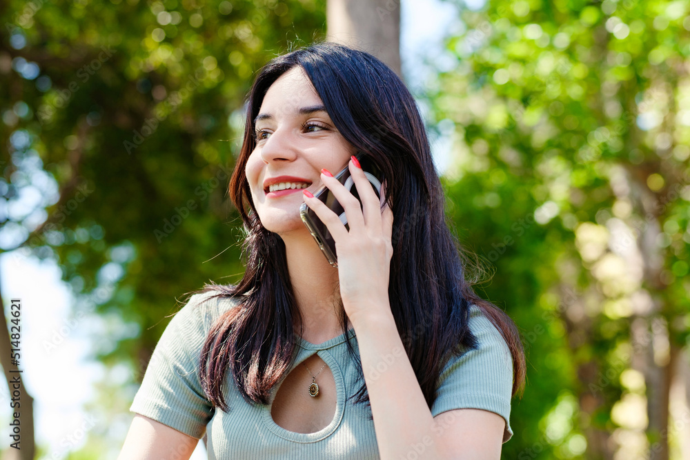 Happy brunette woman wearing turquoise tee on city park, outdoors talking on mobile phone with friends or boyfriend with smiles. Happy brunette woman wearing turquoise tee on city park, outdoors talking on mobile phone with friends or boyfriend with smiles.