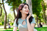 Young beautiful woman wearing turquoise tee on city park, outdoors talking on mobile phone with friends or boyfriend with smiles.