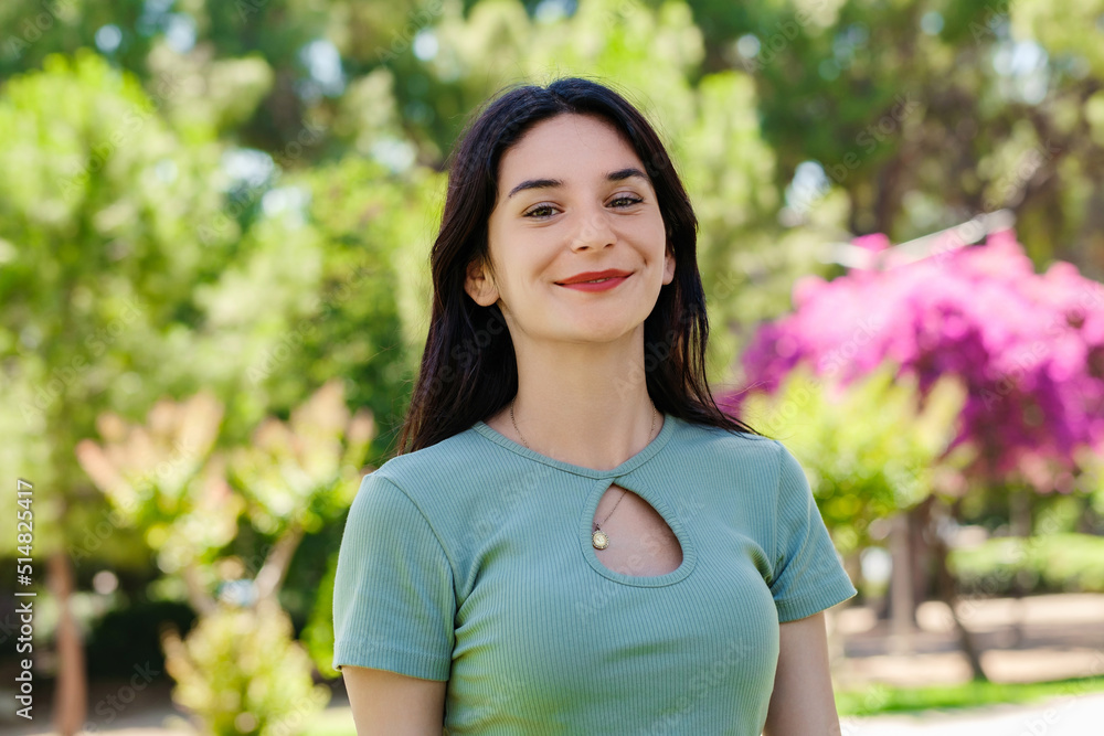 Beautiful brunette woman wearing turquoise t-shirt standing on city park, outdoors looking at camera while posing. Natural beauty concept. Beautiful girl. Pretty young woman.