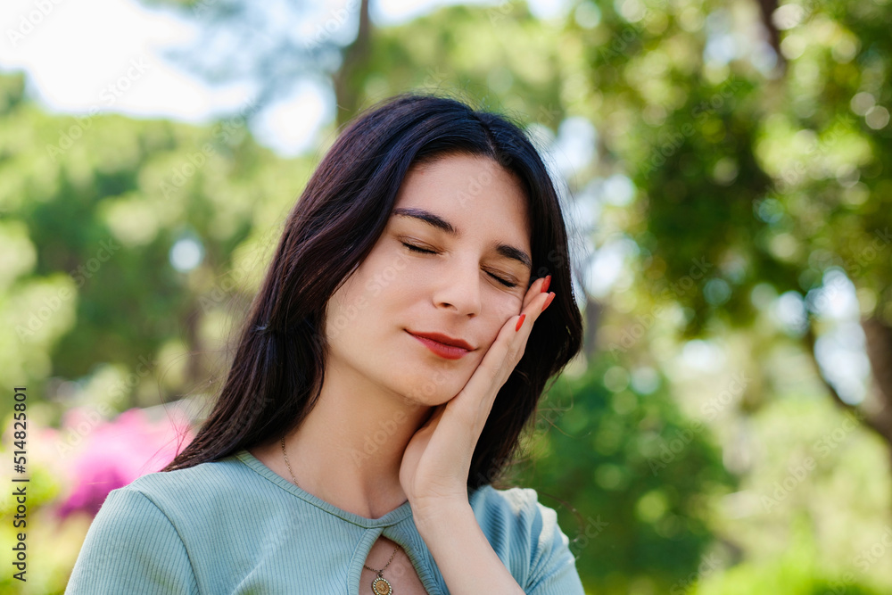 Young caucasian woman wearing tee standing on city park, outdoors touching mouth with hand with painful expression because of toothache or dental illness on teeth. Suffering from sensitive. Young caucasian woman wearing tee standing on city park, outdoors touching mouth with hand with painful expression because of toothache or dental illness on teeth. Suffering from sensitive.
